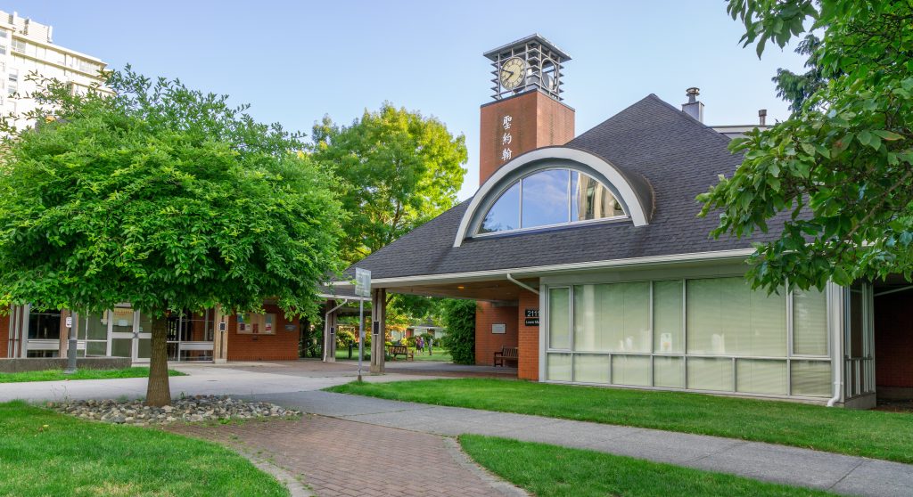 St. John's College building. There is a pointy black roof with a large circular window. A red clock tower with Chinese characters is behind the building.
